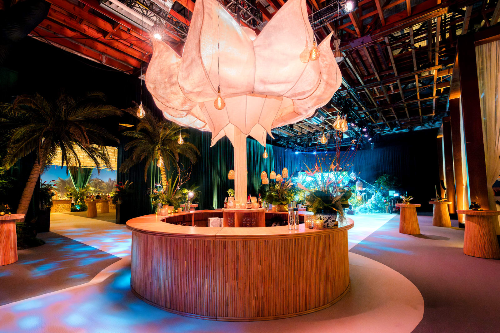 A large fabric lotus chandelier hangs over a round rattan bar ringed with palms at The White Lotus season 3 premiere