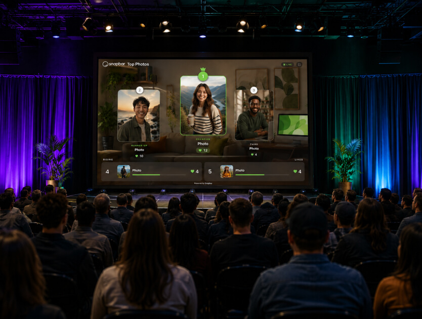 Seated conference audience facing a stage screen that ranks guest photos by vote count with a crowned first place