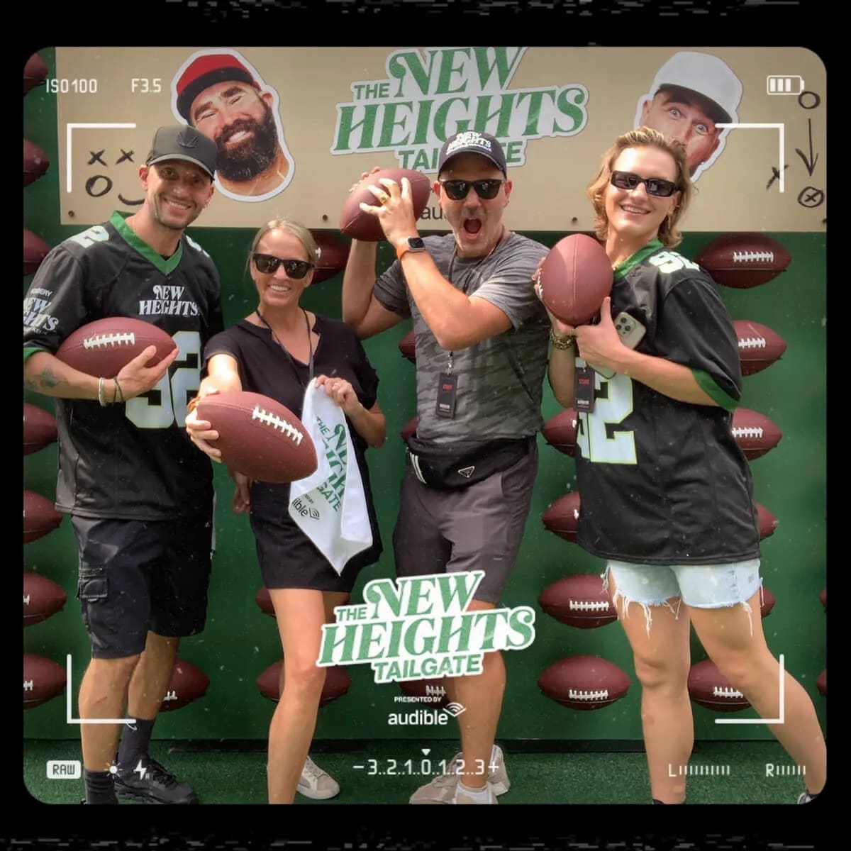 Four fans in football jerseys holding footballs in front of a branded tailgate backdrop, with the event and presenting sponsor's names on the photo frame